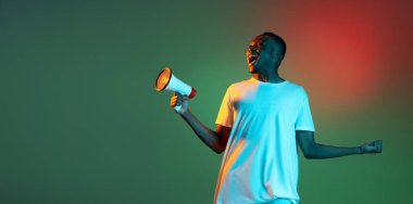 Neon gradyan arka planında hoparlörle poz veren Afrikalı genç bir adam. Duygu, eylem, yüz ifadesi kavramı.