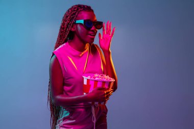 Sinema izliyordum. Mavi stüdyo arka planında neon ışıkta genç Afrikalı kadın portresi. Gençlik kavramı, insan duyguları, yüz ifadesi.