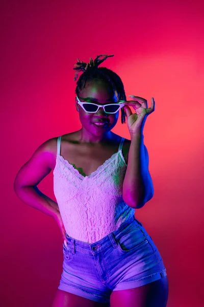 美しいですアフリカの女の子でスタイリッシュな夏服posing絶縁上の明るい色のネオン背景. — ストック写真