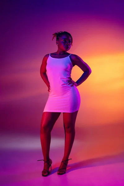 Mooi Afrikaans meisje in wit korte zomer jurk poseren geïsoleerd over heldere kleurrijke neon achtergrond. — Stockfoto