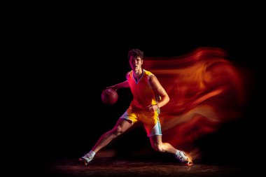 Beyaz tenli profesyonel basketbolcu, siyah arka planda karışık neon ışıklarda tek başına egzersiz yapıyor..