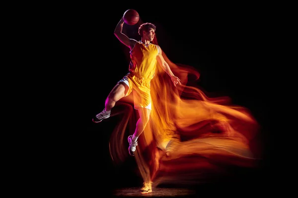 Young Caucasian basketball player training isolated on black background in mixed neon lights.