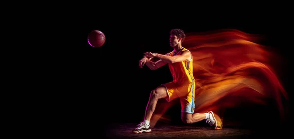 Joven jugador de baloncesto caucásico entrenando aislado sobre fondo negro en luces mixtas de neón. —  Fotos de Stock