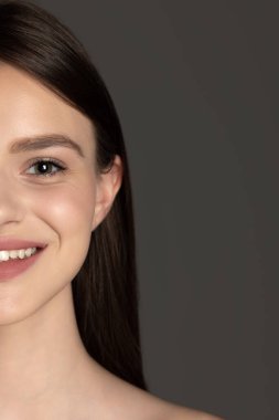 Gri stüdyo arka planında izole edilmiş güzel, gülümseyen bir kızın portresi. Güzellik kavramı, şefkat, duygusallık.