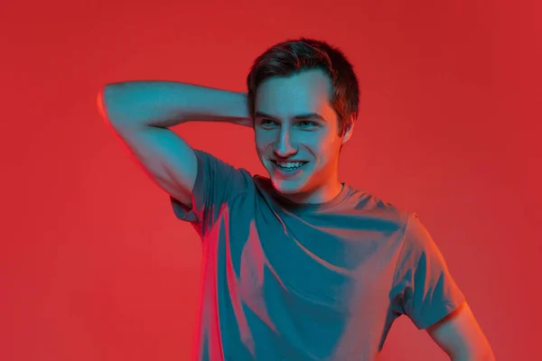 Egy fiatal, mosolygós, jóképű kaukázusi fickó, vörös neon háttérrel elszigetelve. Az emberi érzelmek fogalma, arckifejezés. — Stock Fotó