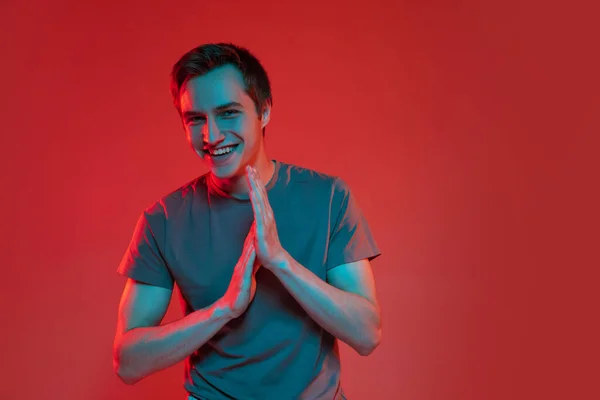 Um belo jovem caucasiano sorridente isolado em fundo de néon vermelho. Conceito de emoções humanas, expressão facial. — Fotografia de Stock