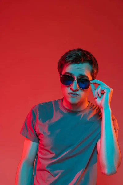 One young handsome caucasian guy in sunglasses isolated on red neon background. Concept of human emotions, facial expression. — Stock Photo, Image
