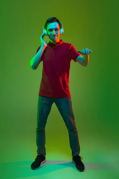 Estúdio imagem de jovem caucasiano em fones de ouvido isolados em fundo verde em luz de néon — Fotografia de Stock