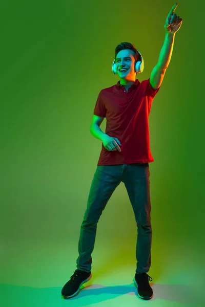 헤드폰을 끼고 네온 빛을 받은 녹색 배경에 고립된 젊은 코카서스 남성의 스튜디오 사진 — 스톡 사진