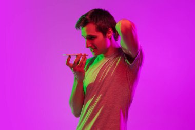 Akıllı telefonlu yakışıklı beyaz adam pembe neon arka planda izole edilmiş. Stüdyo çekimi.