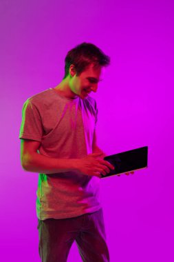 Neon ışıkta pembe arka planda dijital tabletli beyaz bir adamın stüdyo görüntüsü. Duygu, gençlik, satış kavramı
