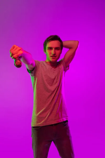 Un joven guapo sonriente con micrófono aislado sobre fondo de neón rosa. Concepto de expresión facial y emociones humanas —  Fotos de Stock