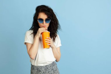 Güneş gözlüklü, açık mavi renkli stüdyo arka planında izole edilmiş beyaz bir kızın stüdyo görüntüsü..