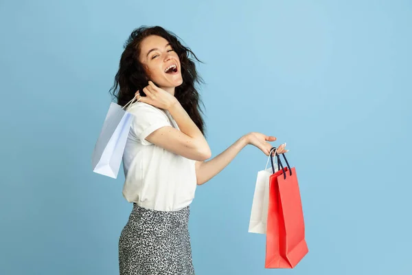 Shopping, vendite. Ritratto di bella giovane ragazza caucasica riccia con sacchetti di carta isolati su sfondo azzurro studio. — Foto Stock