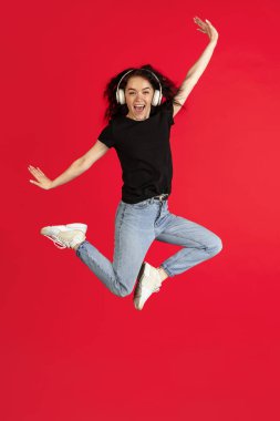 Beyaz kulaklıklı genç bir beyaz kadın kırmızı arka planda yüksek izole atlıyor..