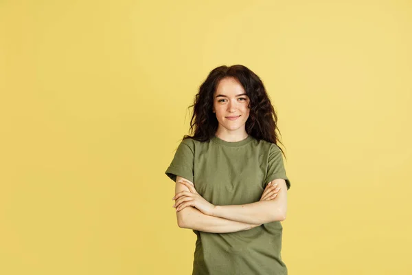 Eine ruhige, lächelnde kaukasische Frau mit verschränkten Armen auf der Brust posiert isoliert vor gelbem Studiohintergrund. — Stockfoto