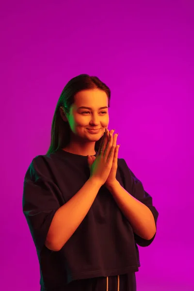 Függőleges portré csinos fiatal mosolygós kaukázusi lány alkalmi ruhák pózol rózsaszín háttér neon fények — Stock Fotó