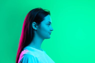 Yeşil arka planda neon ışıkta izole edilmiş güzel, gülümseyen beyaz bir kızın yakın plan portresi. Yan görünüm