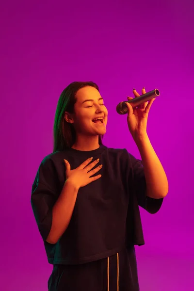 Függőleges portré csinos fiatal kaukázusi lány énekel érzelmileg mikrofonba rózsaszín háttér neon fények — Stock Fotó
