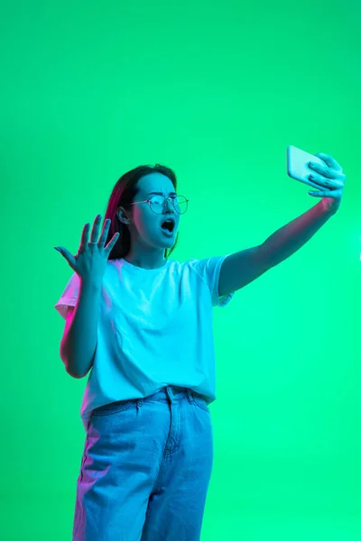 Portrait de joyeuse jeune belle fille, modèle féminin avec smartphone isolé sur fond vert au néon. — Photo