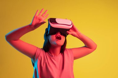 VR gözlüklü, sarı neon arka planda beyaz bir kızın stüdyo fotoğrafı. Sanal gerçeklik ve eğlence kavramı