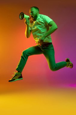 Kafkasyalı genç bir adamın tam boy portresi megafonla atlıyor. Neon ışıklarıyla izole edilmiş turuncu arkaplanda..