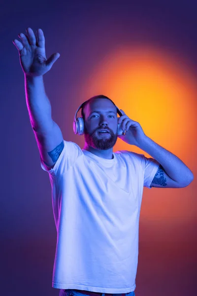 Portrait of young smiling handsome caucasian man in headphones isolated over dark background in neon lights. — Stock Photo, Image