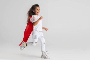 Küçük süper kahraman. Kırmızı pelerinli beyaz kız beyaz stüdyo arka planında izole edilmiş. Yan görünüm