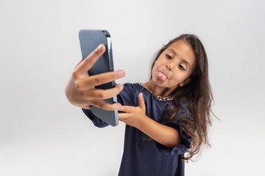 Beyaz stüdyo arka planında izole edilmiş akıllı telefonu tutan güzel elbiseli sevimli bir anaokulu kızının portresi..