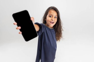 Aygıt ekranı gösteriliyor. Elinde akıllı telefon tutan mavi elbiseli bir anaokulu kızı beyaz stüdyo arka planında izole edilmiş..
