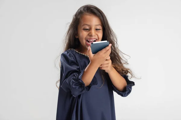 Portrait of one cute Caucasian preschool girl in beautiful blue dress with smartphone isolated over white studio background. — Stock Photo, Image