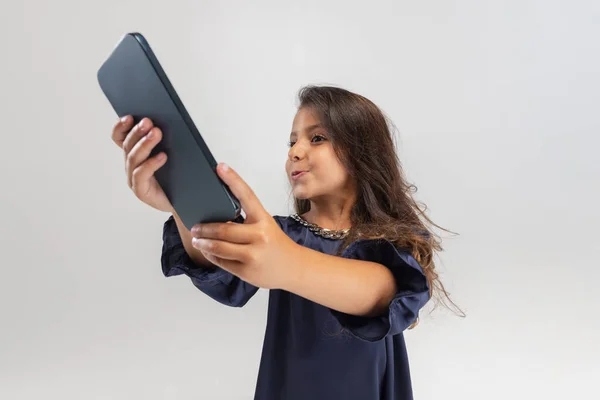 Portrait of one cute smiling preschool girl in beautiful dress holding smartphone isolated over white studio background. — Stock Photo, Image