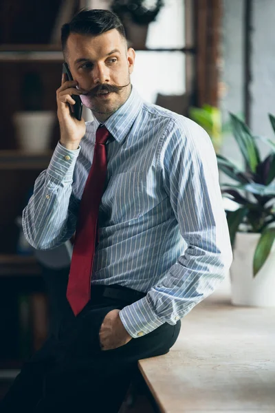 Vertical portrait of young businessman, office worker, manager with smartphone. Modern office interior — Zdjęcie stockowe