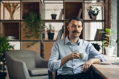 One young smiling businessman, office worker sitting on chair with cup of coffee. Business, working process concept.