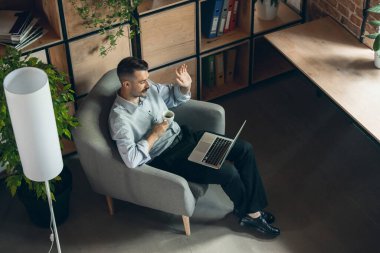One smiling young businessman working on laptop sitting in comfortable armchair. View from above