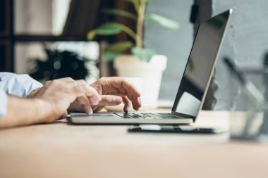 Cropped image of male hands on keyboard of laptop typing text or message. Side view.