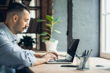 Communicating, chatting. Image of one young caucasian man sitting in front of laptop screen. Side view.