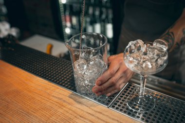 Ice in the glasses. One professional bartender mixing cocktails with long spoon in pub or cafe. Close-up image