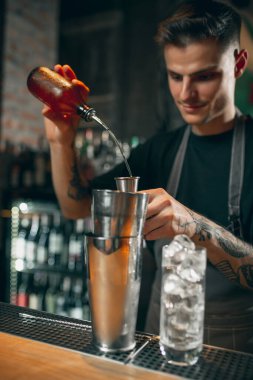 One young handsome bartender shaking an alcohol drink in cocktail shaker enjoying his job.