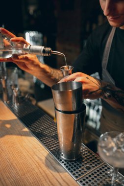 Close up. One young handsome bartender preparing an alcohol drink in cocktail shaker standing behind bar counter