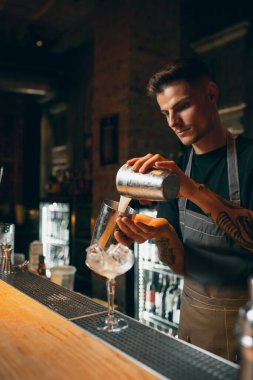 One professional bartender shaking an alcohol drink in cocktail shaker enjoying his job.