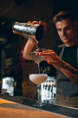 Preparing cocktail for woman. One professional bartender pouring alcohol drink into glass for margarita.
