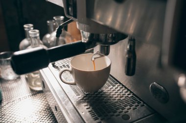 Fresh aromatic hot coffee flows from the coffee machine into a white cup. Close up image