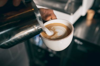 Barista pouring milk into a cup of coffee, sweet cappuchino or latte. Close up image