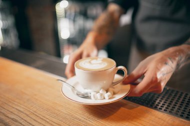 White cup of coffee, latte or cappuchino with marshmallow on wooden bar counter in cafe. Close up