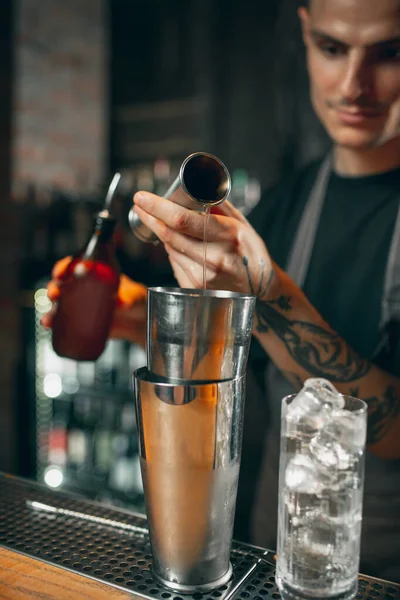 Cropped image of young handsome bartender shaking an alcohol drink in cocktail shaker enjoying his job.