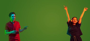 Portraits of two young smiling joyful people, man and woman dancing to music over green background. Collage