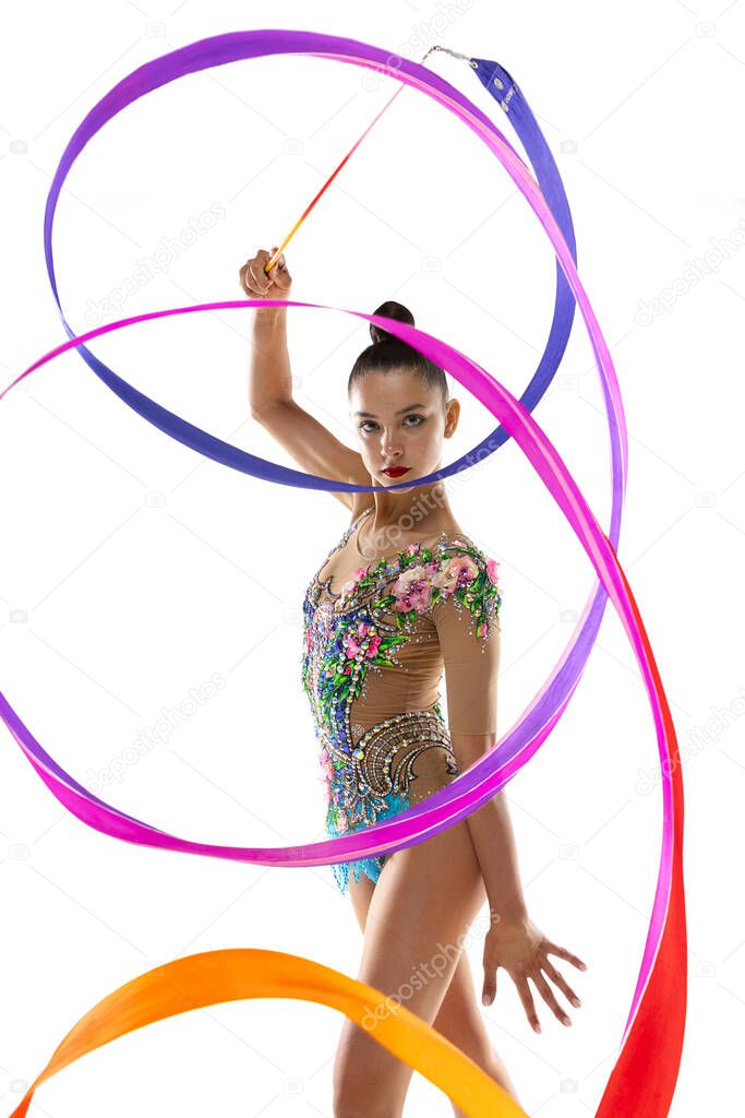 Vertical portrait of female rhythmic gymnast in motion and action with bright ribbon isolated on white studio background.