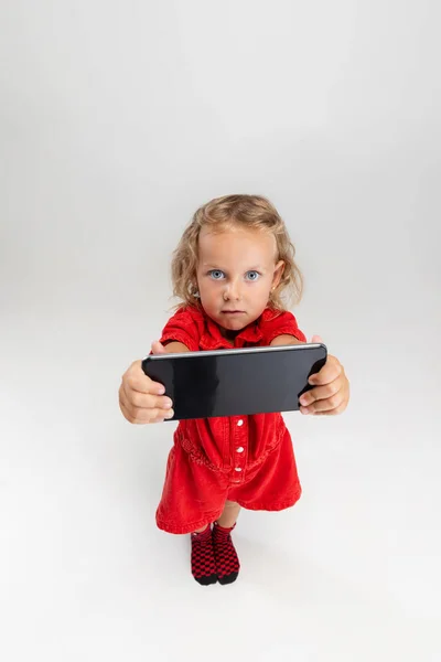 Showing device screen. One little screaming preschool girl holding smartphone isolated over white studio background. — Stock Photo, Image