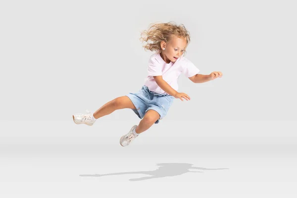 Estúdio tiro de pequena menina caucasiana pré-escolar em roupas casuais caindo isolado sobre fundo estúdio branco. — Fotografia de Stock